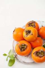 A bunch of ripe persimmons in a bowl on a white table
