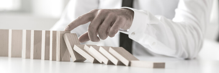 Wide cropped view of a businessman stopping domino effect