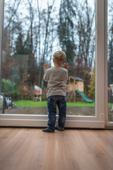 Single blond child standing on a wooden floor at home in front of a window