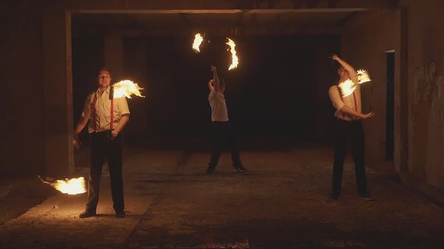 Group of male artists performing fire show at dark in slow motion.