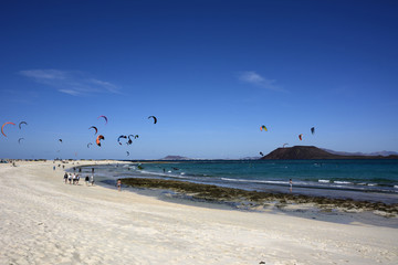 Strand Szene mit Kite Surfern und Spaziergängern.
