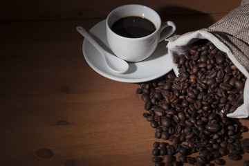 White cup with italian espresso coffee on wooden table with roasted coffee beans