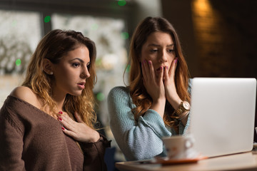 Two shocked female friends reading something on a laptop.