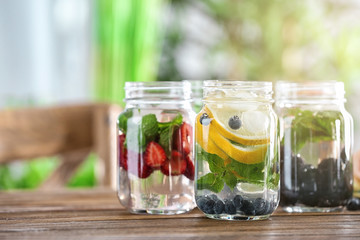 Mason jars of infused water with fruits and berries on wooden table