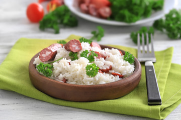 Wooden plate with rice and sausage on fabric