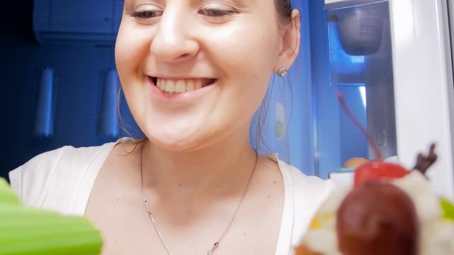 4k footage of young smiling woman looking inside of refrigerator at night and taking out celery