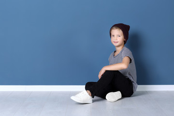 Obraz premium Cute fashionable boy sitting on floor near color wall