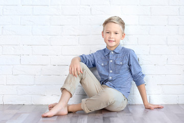 Cute fashionable boy sitting on floor near white brick wall