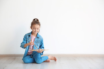 Little girl with watercolors and brush against white wall indoors