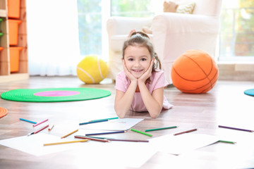 Little girl with color pencils and paper lying on floor at home