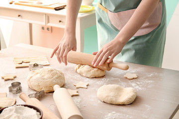 Woman rolling out puff pastry at table in kitchen
