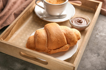 Tray with yummy croissant and cup of coffee on table