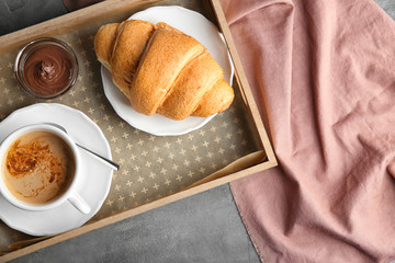 Tray with yummy croissant and cup of coffee on table