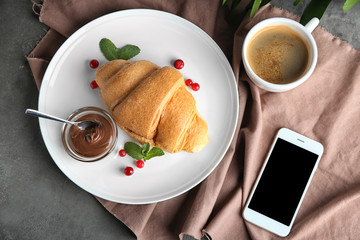 Composition with yummy fresh croissant and mobile phone on table