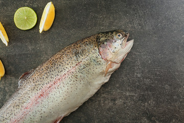 Raw rainbow trout, lemon and lime on grey background, top view