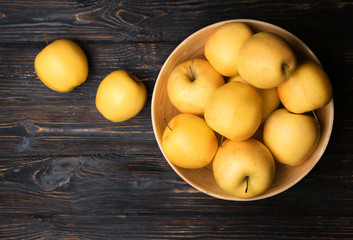 Wooden bowl with ripe yellow apples on table