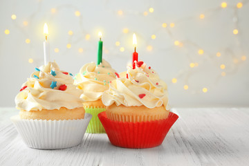 Tasty cupcakes with candles on wooden table