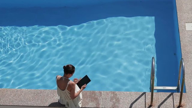 Top view of woman using her tablet on pool edge on a sunny day