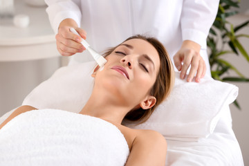 Obraz na płótnie Canvas Beautician applying cream on young woman's face in spa salon