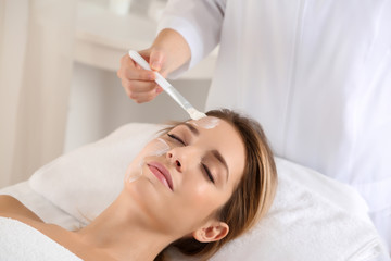 Beautician applying cream on young woman's face in spa salon