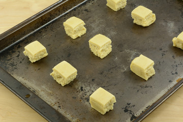 Pre-cut sugar cookie dough cubes arranged on baking pan in preparation for baking