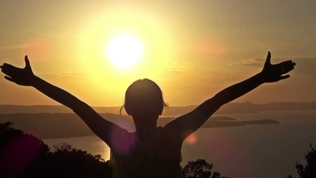 Free happy woman raising arms watching the sun in the background at sunset