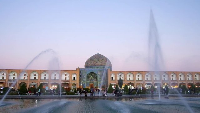 The patterned dome and bright blue tiled portal (iwan) of Sheikh Lotfollah Mosque behind the fountains in crowded Naqsh-e Jahan square, Isfahan, Iran