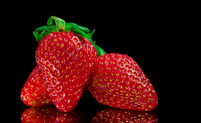 Red Strawberries with green leafs, on top of a reflective glass surface, and black background, isolated.