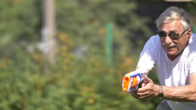 Senior man in a toy gun fight on nature, slow motion