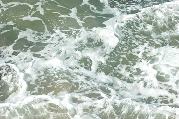 An abstract pattern of white water from waves. The water is shallow, and the sandy ocean floor is visible.