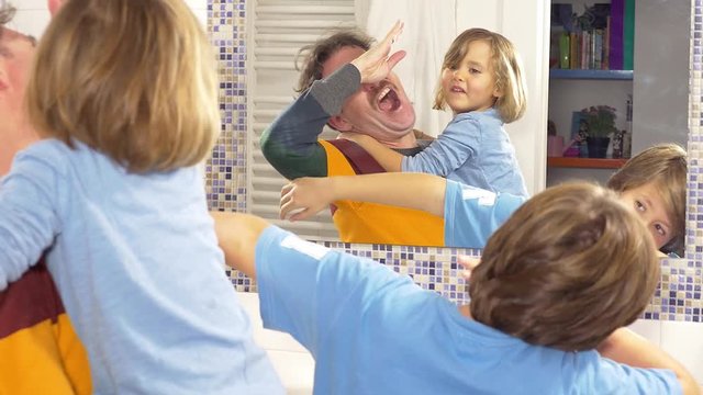 Man dancing with little daughter and son in bathroom in front of mirror