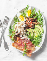 Boiled chicken, avocado, egg, arugula, kumato tomato, bacon salad on a light background, top view