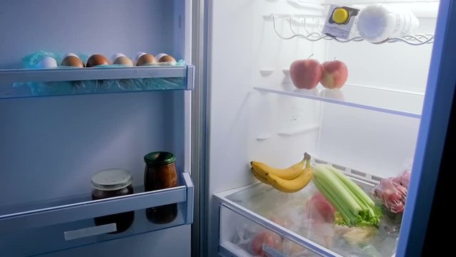 Panning footage of open refrigerator full of food at night