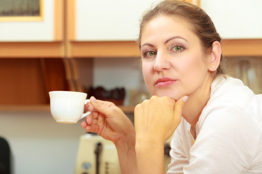 Mature woman holding cup of coffee in kitchen.