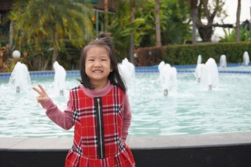 asian kid girl smiling and posting on beautiful of fountain splash 