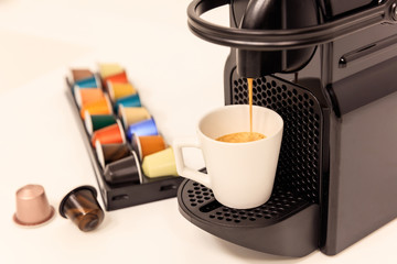 Espresso machine in black color prepares espresso coffee, capsules around. Close up view, details.