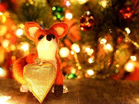 Fox toy. Love heart. New years greetings background. Fancy handmade toy from wool on bokeh Christmas background. Copyspace for congratulations.