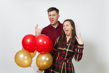 Fototapeta na wymiar Crazy fun European young happy smiling couple in love. Woman and man in plaid checkered clothes with red, yellow balloons, doing rock gesture, on white background isolated. Holiday, party concept.