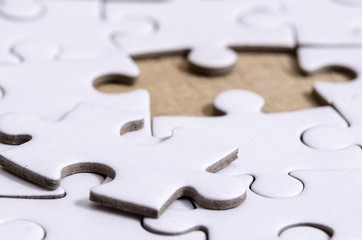 the last gap and its solution, close up of a white jigsaw/puzzle whit one gap, over wooden table...