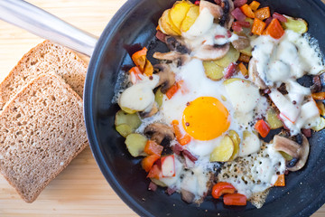 Deftiges Frühstück mit Spiegelei, Kartoffeln, Paprika, Champignons und Käse in der Pfanne