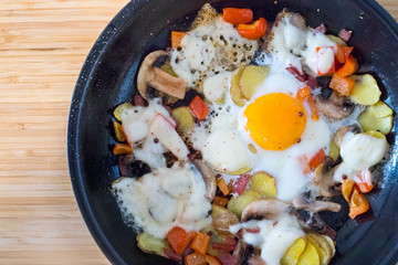 Deftiges Frühstück mit Spiegelei, Kartoffeln, Paprika, Champignons und Käse in der Pfanne