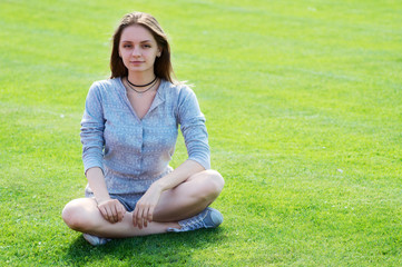 A beautiful young woman sits on a green lawn of a grass at a sports stadium.