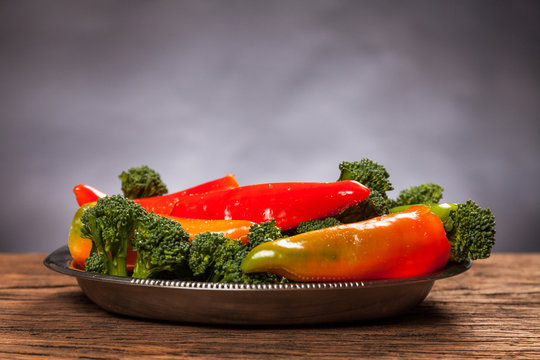 Fresh red pepperoni frigitelli and broccoli on a wooden table. Dark background. Vegan food