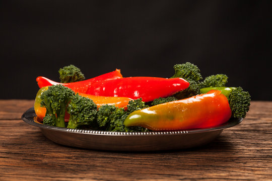 Fresh red pepperoni frigitelli and broccoli on a wooden table. Dark background. Vegan food
