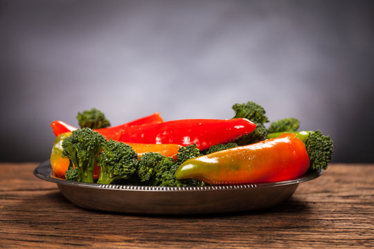 Fresh red pepperoni frigitelli and broccoli on a wooden table. Dark background. Vegan food