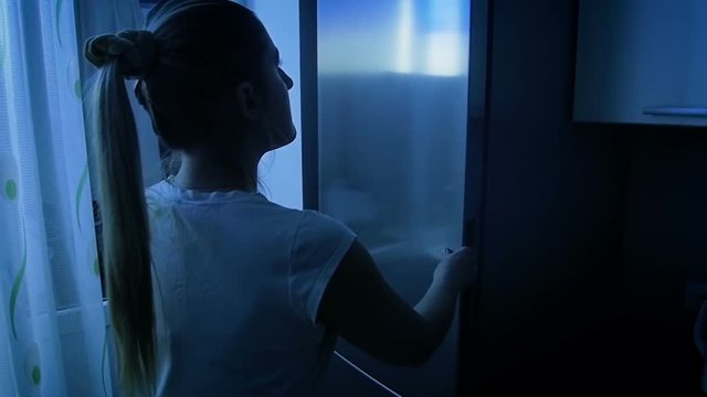 Slow motion video of young woman taking bottle of milk from refrigerator at night