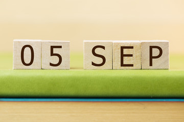 Wooden cube shape calendar for SEP 5 on green book, table.