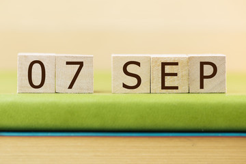 Wooden cube shape calendar for SEP 7 on green book, table.