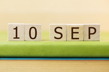 Wooden cube shape calendar for SEP 10 on green book, table.