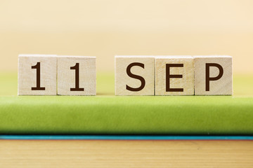 Wooden cube shape calendar for SEP 11 on green book, table.